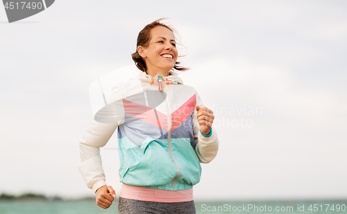 Image of smiling woman running along beach