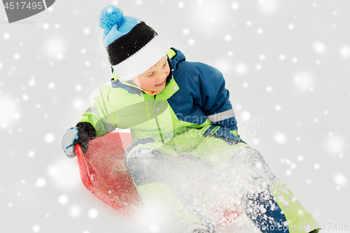 Image of happy boy sliding on sled down snow hill in winter