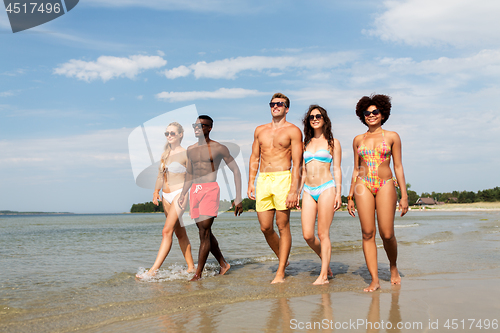 Image of happy friends walking along summer beach