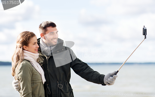 Image of happy couple taking selfie on beach in autumn