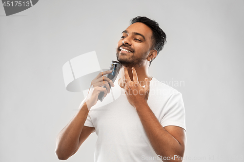 Image of smiling indian man shaving beard with trimmer