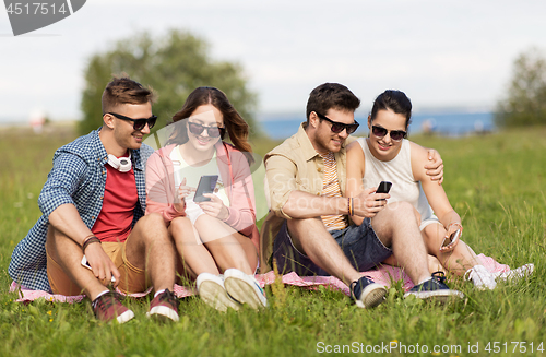 Image of smiling friends with smartphones sitting on grass