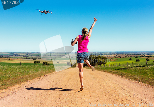 Image of Woman leaping for joy along dirt road flying a drone