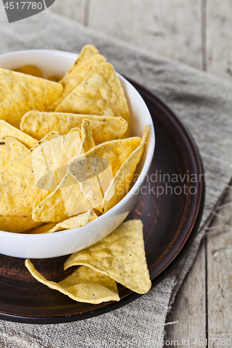 Image of Mexican nachos chips in white bowl on brown ceramic plate closeu