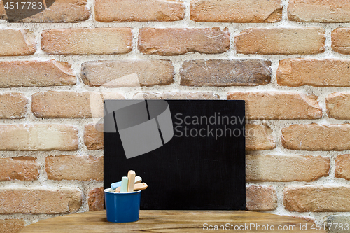 Image of Blank clean blackboard an chalk on wooden table at brick wall. 