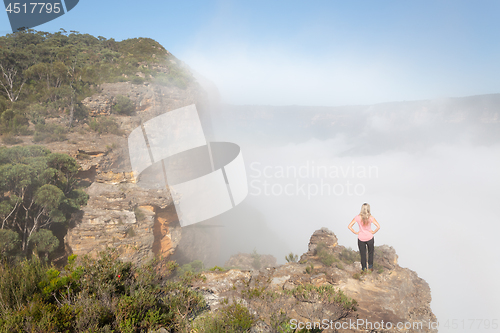 Image of Female hiker standing on a rock pinnacle with rising fog from valley