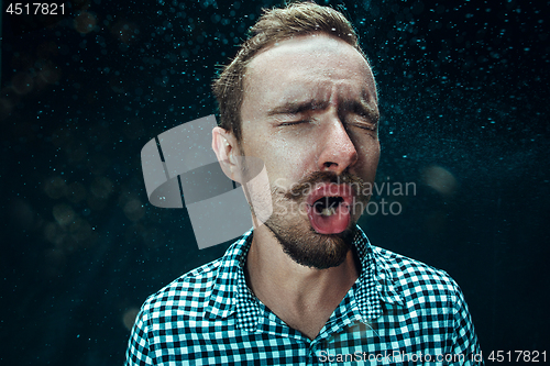 Image of Young handsome man with beard sneezing, studio portrait