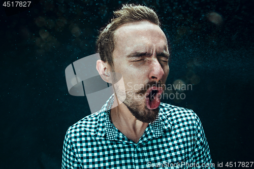 Image of Young handsome man with beard sneezing, studio portrait