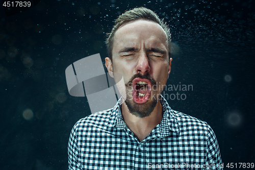 Image of Young handsome man with beard sneezing, studio portrait