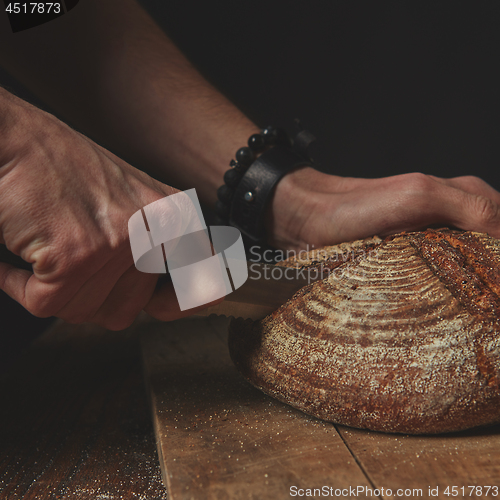 Image of man cuts a round dark bread