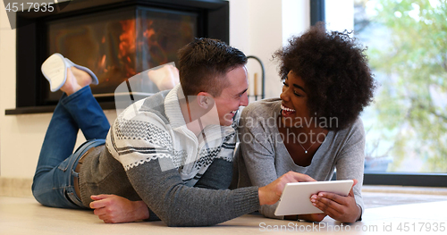 Image of multiethnic couple using tablet computer on the floor