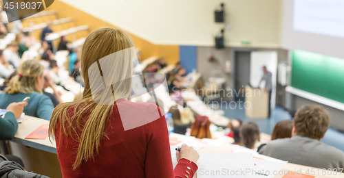 Image of Audience in the lecture hall. Female student making notes.