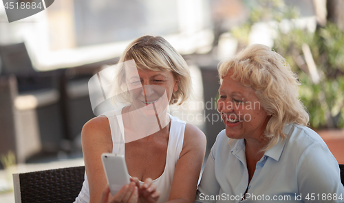 Image of Two middle aged women sitting outside and smiling while looking at a smartphone screen