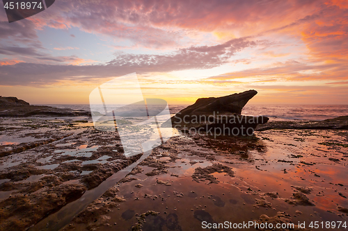 Image of Sunrise on coastal beach rock shelf with reflections low tide