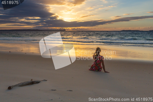 Image of Female sitting on the sand watching the sunrise