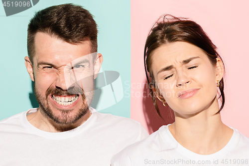 Image of Closeup portrait of young couple, man, woman. One being excited happy smiling, other serious, concerned, unhappy on pink and blue background. Emotion contrasts