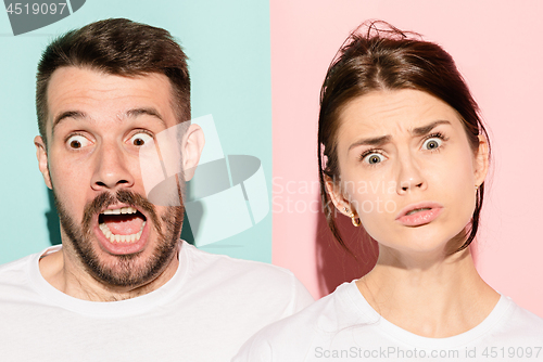 Image of Closeup portrait of young couple, man, woman. One being excited happy smiling, other serious, concerned, unhappy on pink and blue background. Emotion contrasts