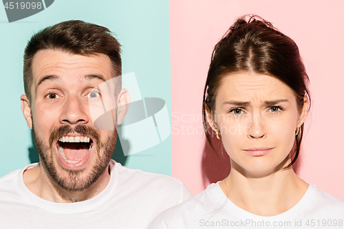 Image of Closeup portrait of young couple, man, woman. One being excited happy smiling, other serious, concerned, unhappy on pink and blue background. Emotion contrasts