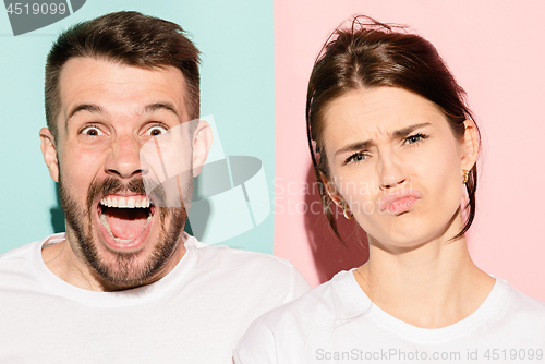 Image of Closeup portrait of young couple, man, woman. One being excited happy smiling, other serious, concerned, unhappy on pink and blue background. Emotion contrasts