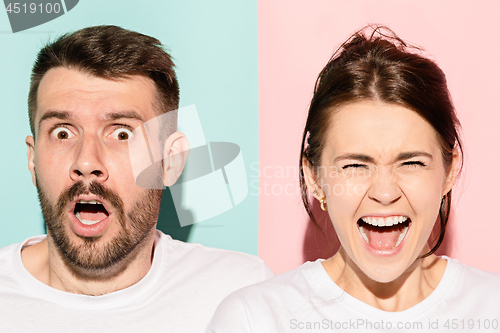 Image of Closeup portrait of young couple, man, woman. One being excited happy smiling, other serious, concerned, unhappy on pink and blue background. Emotion contrasts