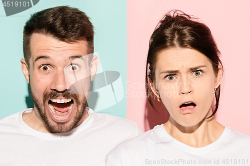 Image of Closeup portrait of young couple, man, woman. One being excited happy smiling, other serious, concerned, unhappy on pink and blue background. Emotion contrasts