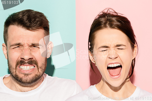 Image of Closeup portrait of young couple, man, woman. One being excited happy smiling, other serious, concerned, unhappy on pink and blue background. Emotion contrasts