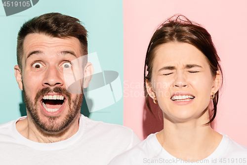 Image of Closeup portrait of young couple, man, woman. One being excited happy smiling, other serious, concerned, unhappy on pink and blue background. Emotion contrasts