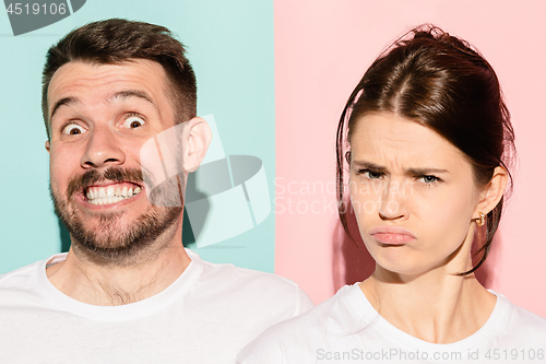 Image of Closeup portrait of young couple, man, woman. One being excited happy smiling, other serious, concerned, unhappy on pink and blue background. Emotion contrasts