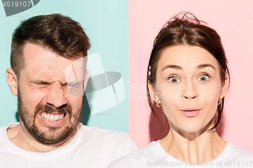 Image of Closeup portrait of young couple, man, woman. One being excited happy smiling, other serious, concerned, unhappy on pink and blue background. Emotion contrasts