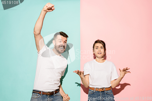 Image of Closeup portrait of young couple, man, woman. One being excited happy smiling, other serious, concerned, unhappy on pink and blue background. Emotion contrasts