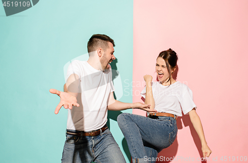 Image of Closeup portrait of young couple, man, woman. One being excited happy smiling, other serious, concerned, unhappy on pink and blue background. Emotion contrasts