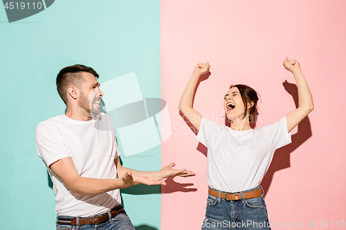 Image of Closeup portrait of young couple, man, woman. One being excited happy smiling, other serious, concerned, unhappy on pink and blue background. Emotion contrasts