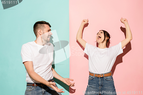 Image of Closeup portrait of young couple, man, woman. One being excited happy smiling, other serious, concerned, unhappy on pink and blue background. Emotion contrasts