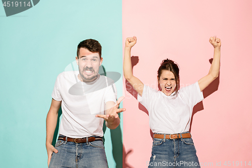 Image of Closeup portrait of young couple, man, woman. One being excited happy smiling, other serious, concerned, unhappy on pink and blue background. Emotion contrasts