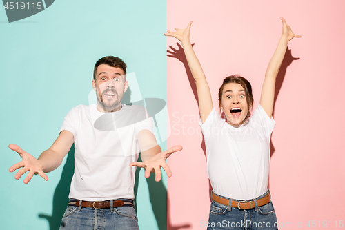 Image of Closeup portrait of young couple, man, woman. One being excited happy smiling, other serious, concerned, unhappy on pink and blue background. Emotion contrasts