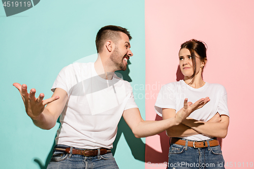 Image of Closeup portrait of young couple, man, woman. One being excited happy smiling, other serious, concerned, unhappy on pink and blue background. Emotion contrasts