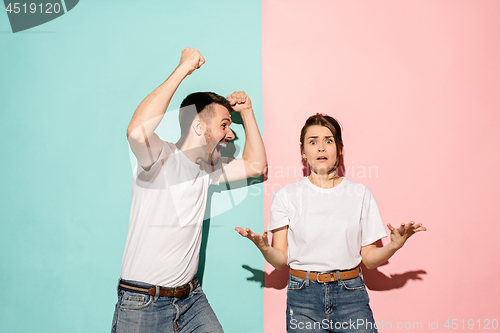 Image of Closeup portrait of young couple, man, woman. One being excited happy smiling, other serious, concerned, unhappy on pink and blue background. Emotion contrasts