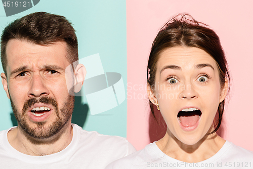 Image of Closeup portrait of young couple, man, woman. One being excited happy smiling, other serious, concerned, unhappy on pink and blue background. Emotion contrasts