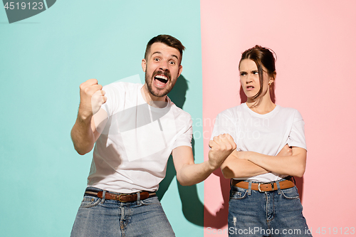 Image of Closeup portrait of young couple, man, woman. One being excited happy smiling, other serious, concerned, unhappy on pink and blue background. Emotion contrasts