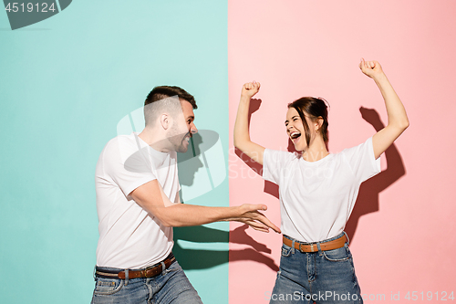 Image of Closeup portrait of young couple, man, woman. One being excited happy smiling, other serious, concerned, unhappy on pink and blue background. Emotion contrasts