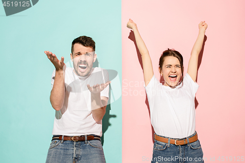 Image of Closeup portrait of young couple, man, woman. One being excited happy smiling, other serious, concerned, unhappy on pink and blue background. Emotion contrasts