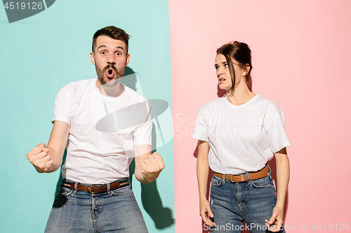 Image of Closeup portrait of young couple, man, woman. One being excited happy smiling, other serious, concerned, unhappy on pink and blue background. Emotion contrasts