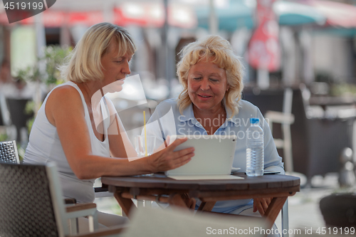 Image of Senior women relaxing in cafe and using digital tablet