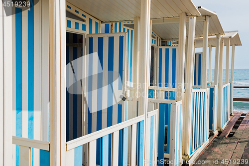 Image of Striped white and blue striped beach houses and black sandy beach.