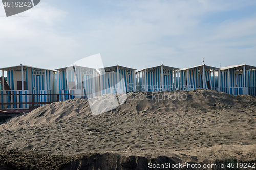 Image of Striped white and blue striped beach houses and black sandy beach.
