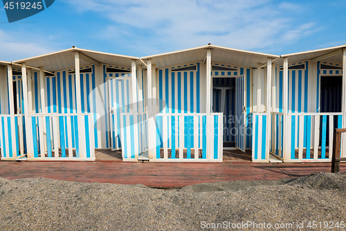 Image of Striped white and blue striped beach houses and black sandy beach.