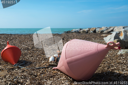 Image of Two big buoys on the beach, azure sea and the rocky beach