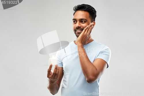 Image of happy indian man applying lotion to face