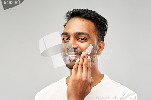 Image of happy indian man applying cream to face