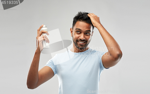 Image of smiling indian man applying hair spray over gray